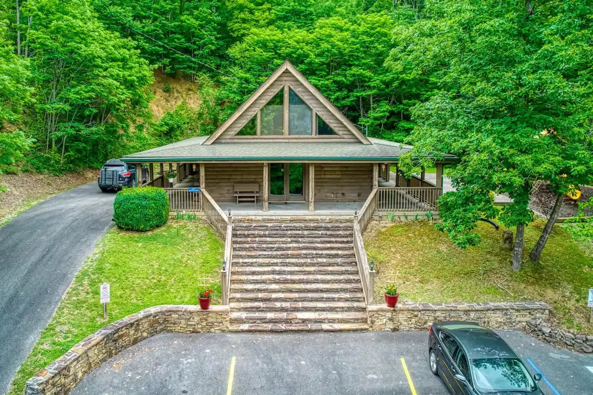 An inviting entrance to the property featuring stone steps, a striking triangular roof structure, and lush surrounding greenery. The image showcases the transition from the outdoors to the welcoming retreat within, hinting at the adventures and gatherings that await.