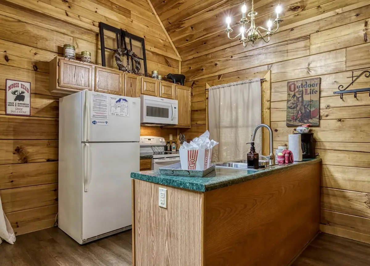 A view of the kitchen cabinetry and countertops, with inviting wooden finishes, a striking green countertop, a decorative chandelier, and artful wall decor. The image radiates warmth and highlights the rustic character that blends with practical kitchen design.