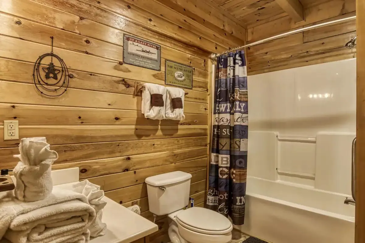 The image centers on a bathroom with warm wooden walls, a bathtub, neatly folded towels, and a shower curtain. The scene exudes a sense of relaxation and comfort, perfect for unwinding after a day of adventure.