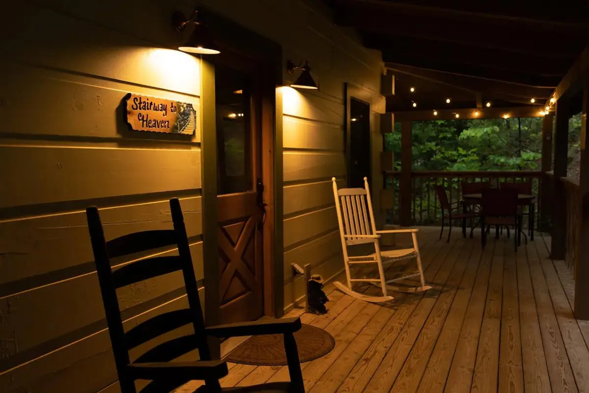 A pair of classic wooden rocking chairs on a porch outside the cabin, strung with warm lights and facing the peaceful outdoors. The inviting setup is perfect for quiet conversations, sunset watching, or stargazing together.