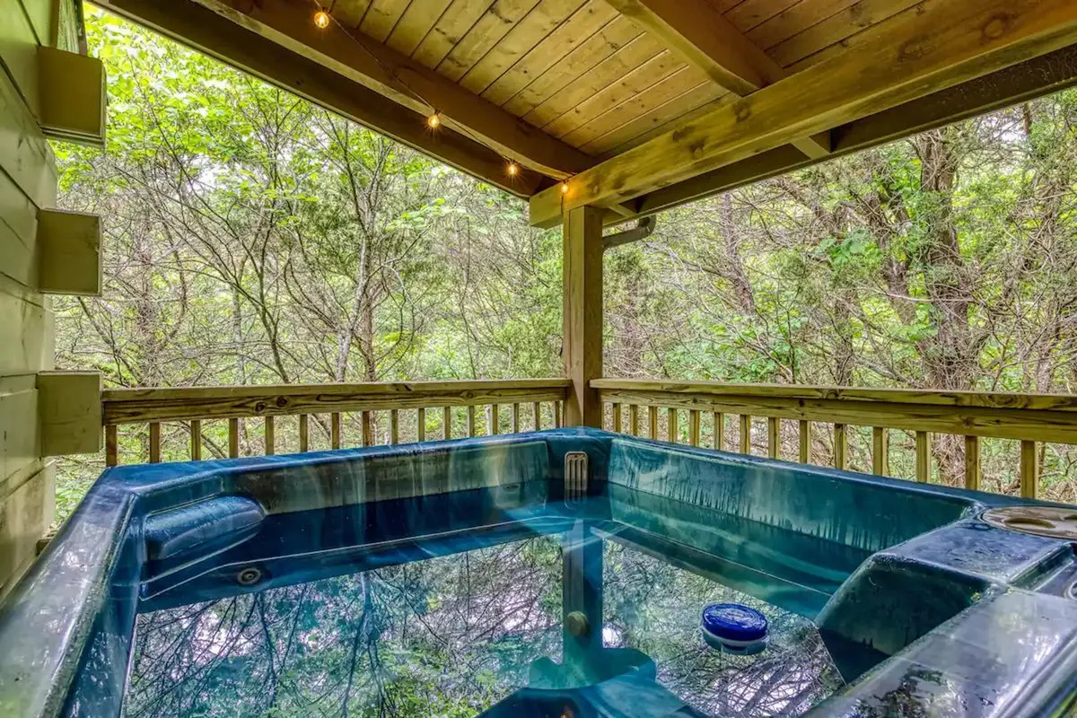 A private outdoor hot tub nestled under a wooden ceiling, surrounded by lush greenery. The setup offers an inviting spot for relaxation and connection, blending comfort with the immersive experience of nature just steps away.