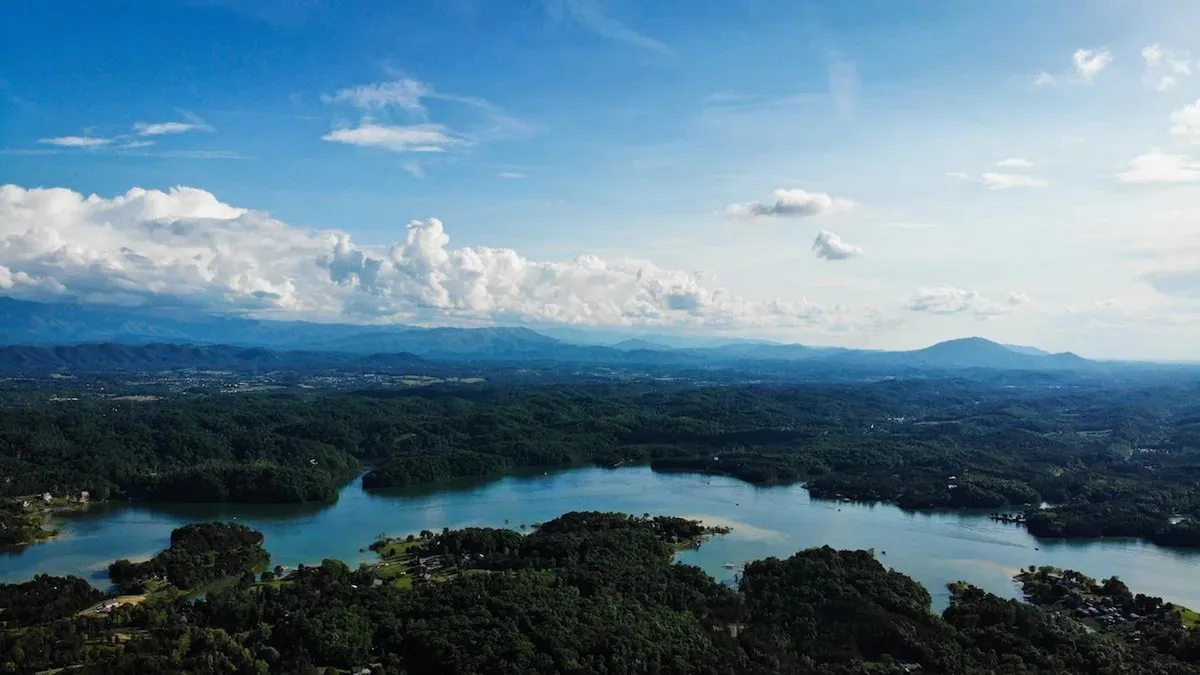 A sweeping view of a tranquil lake with mountains and clouds forming a dramatic backdrop. The clear water reflects the sky, and the surrounding landscape suggests opportunities for hiking, boating, and fishing. The serene setting evokes a sense of adventure and peace, perfectly aligning with outdoor exploration and nature immersion.