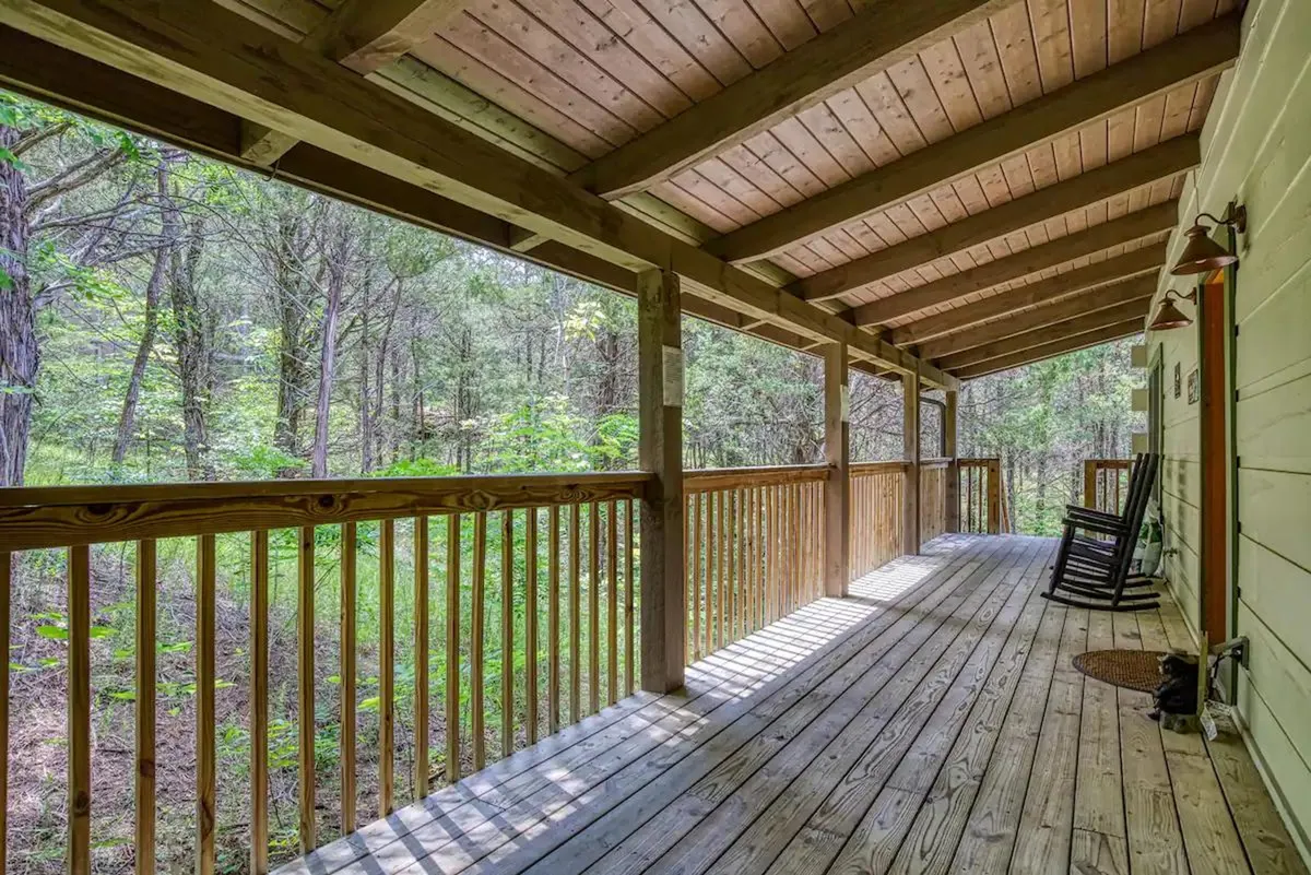 A peaceful porch scene with a wooden railing, a classic rocking chair, wooden flooring, and lush greenery all around. The space is designed for guests to relax, enjoy scenic views, and socialize outdoors.