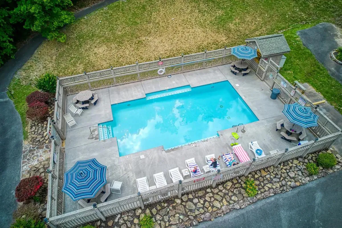 A sparkling community swimming pool surrounded by comfy lounge chairs, umbrellas for shade, and lush greenery, inviting guests for a swim or to relax poolside. The scene exudes a social yet peaceful mood, promising fun and relaxation for all ages.