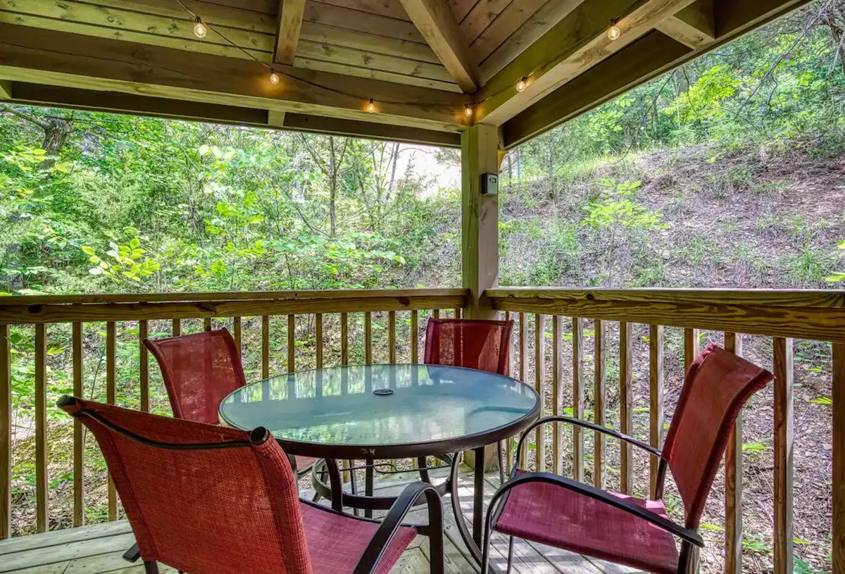 A welcoming outdoor seating area set with a round glass table and comfortable chairs, nestled in nature. The view opens up to trees and greenery, making it a perfect spot for morning coffee, casual meals, or unwinding in the evening breeze.