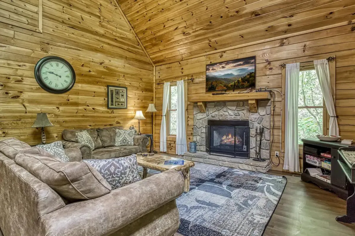 A cozy living space featuring a central fireplace, plush sofas, a television, and expansive windows that frame beautiful views. The setting is warm and intimate, ideal for movie nights, storytelling, and peaceful mornings alike.